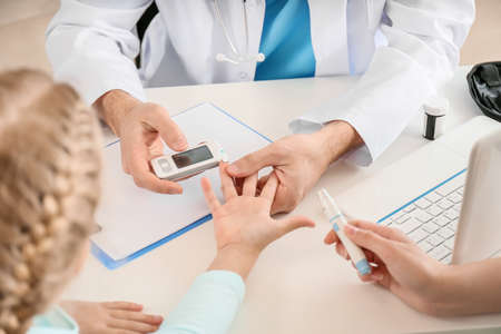 Doctor measuring blood sugar level of little girl in clinicの写真素材