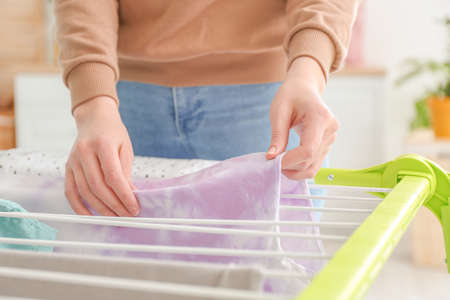 Young woman hanging clean laundry on clothes dryer after washing, closeup