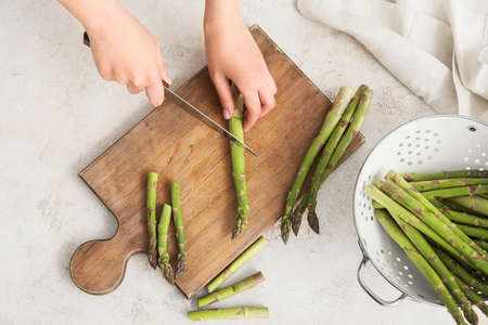 Woman cutting fresh asparagus at tableの写真素材