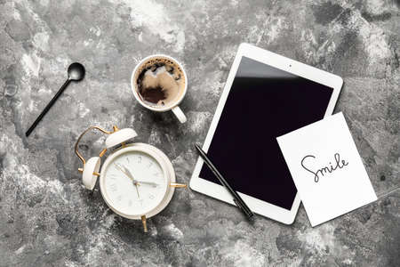 Composition with cup of coffee, tablet computer and alarm clock on gray background