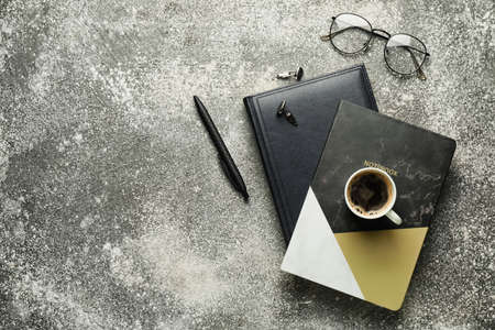 Cup of coffee with stationery and eyeglasses on gray background
