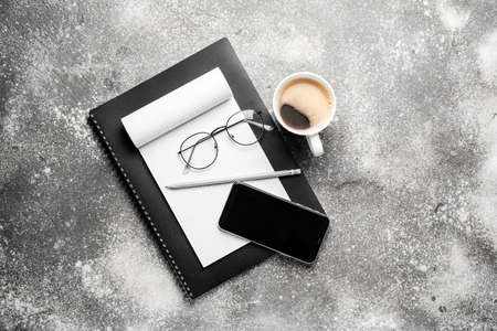 Cup of coffee with stationery, mobile phone and eyeglasses on gray background