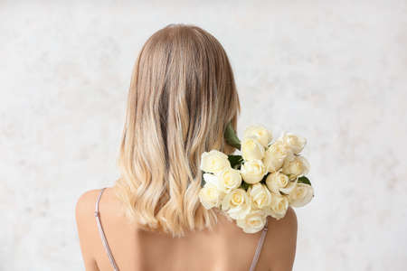 Beautiful young woman with bouquet of roses on light backgroundの写真素材