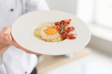 Male chef with tasty pasta carbonara in kitchen, closeupの写真素材