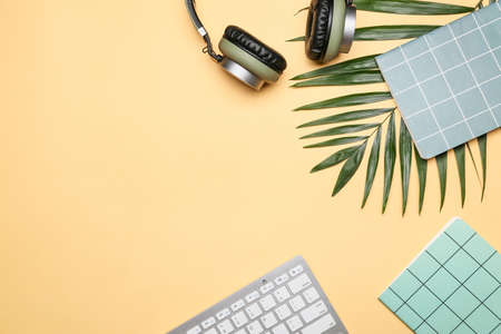 Computer keyboard with headphones and notebooks on color background
