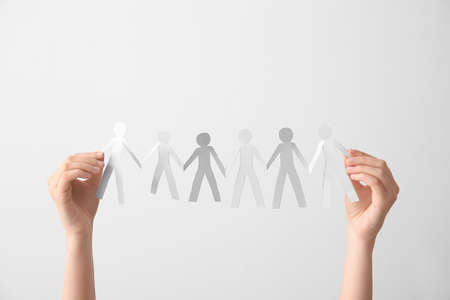 Female hands holding paper human figures on light background. Unity concept