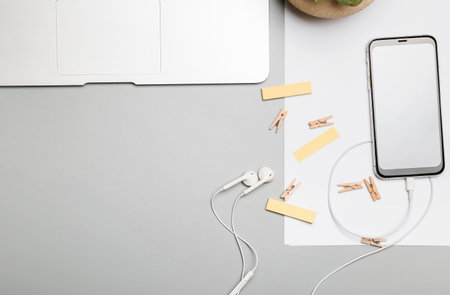 Mobile phone with stationery and earphones on gray background