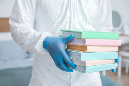 Man in biohazard suit and with books at home, closeup