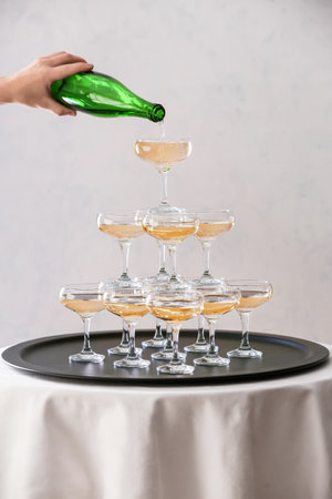Waiter with bottle and tower made of glasses with champagne on tableの写真素材