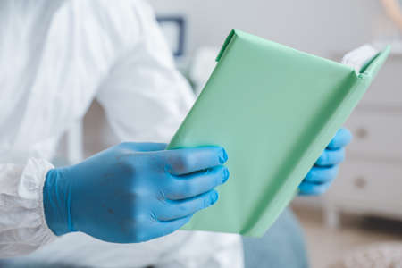 Man in biohazard suit reading book at home, closeupの写真素材