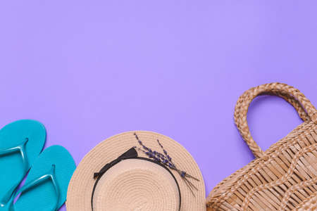 Straw hat and bag with flip-flops on color background