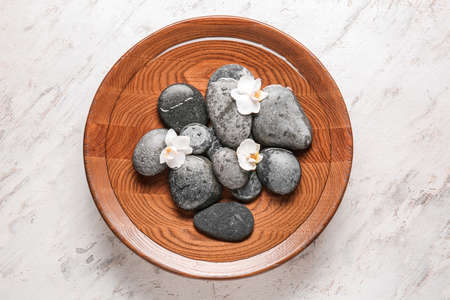 Plate with water, spa stones and flowers on light backgroundの写真素材