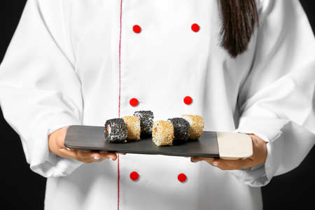 Beautiful Asian chef with sushi rolls on dark background, closeupの写真素材