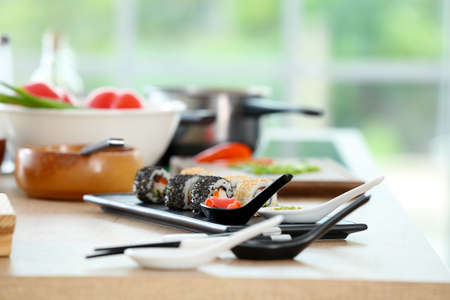 Plate with tasty sushi rolls on table in kitchenの写真素材