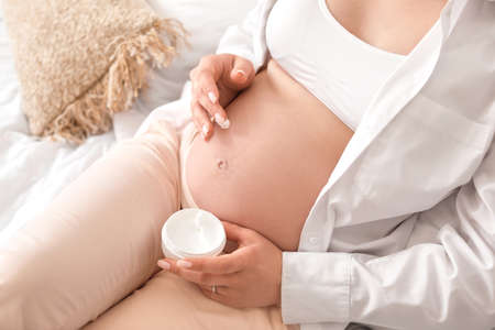 Beautiful pregnant woman with cream at homeの写真素材