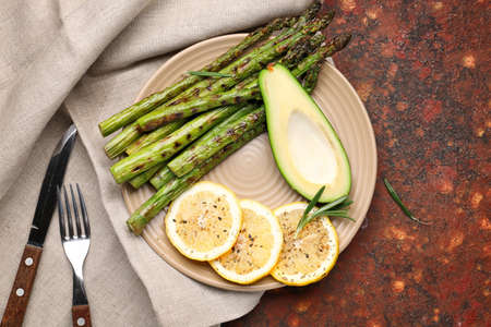 Cooked asparagus with avocado and lemon on color background
