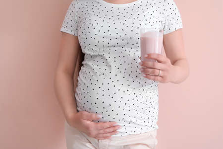 Beautiful pregnant woman with yogurt on color background