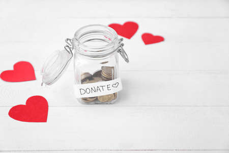 Glass jar with coins and red hearts on table. Concept of donations