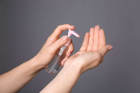 Woman using sanitizer on gray background