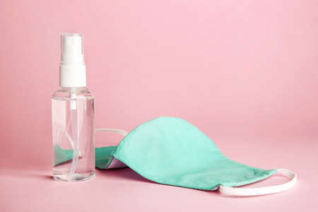Bottle of disinfectant and medical mask on color background