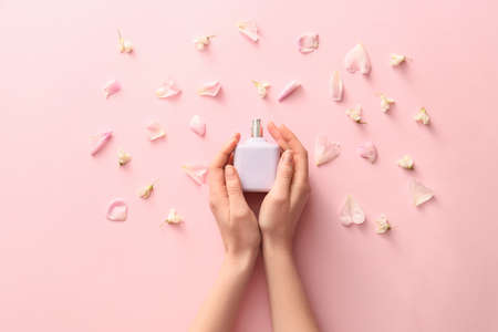 Female hands with floral perfume on color background