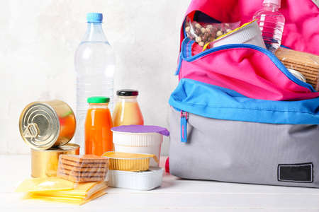 Schoolbag with different products on table. Concept of Backpack Food Programの写真素材
