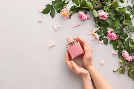 Female hands with perfume and flowers on light backgroundの写真素材