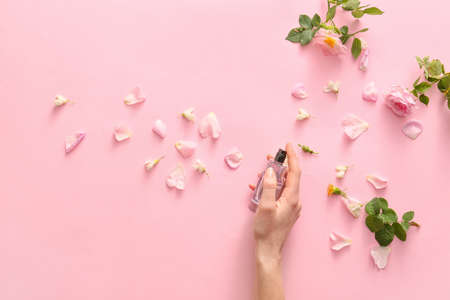 Female hand with perfume and flowers on color backgroundの写真素材