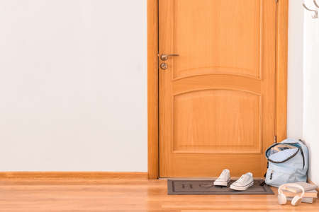 Door mat with backpack and shoes on floor in hallwayの写真素材