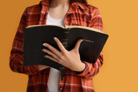 Young woman with Bible on color background