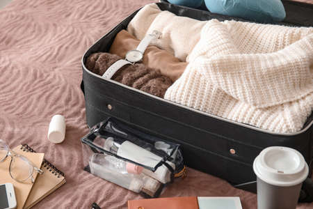 Suitcase with female clothes and accessories on bed