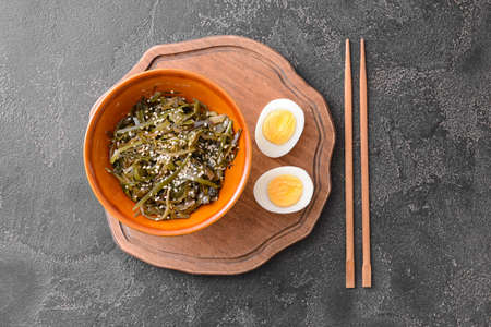 Bowl with tasty seaweed, boiled egg and chopsticks on gray background