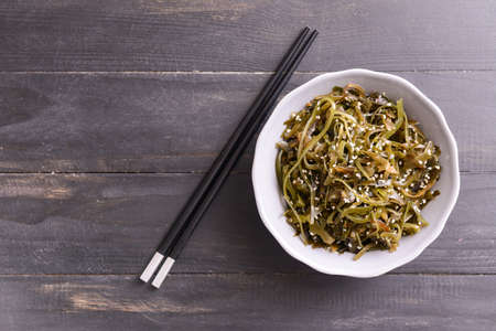 Bowl with tasty seaweed and chopsticks on wooden backgroundの写真素材