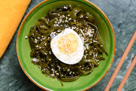 Bowl with tasty seaweed, boiled egg and chopsticks on table