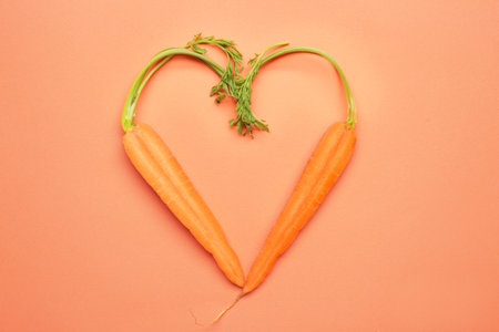 Heart shape made of cut carrot on color background