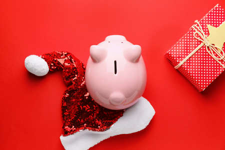 Piggy bank, Christmas gift and Santa hat on color backgroundの写真素材