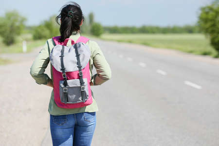 Female traveler with backpack walking along the roadの写真素材