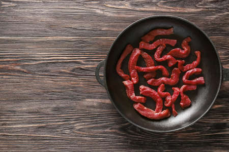 Frying pan with pieces of fresh beef meat on wooden background