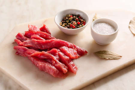 Pieces of fresh beef meat with spices on light background