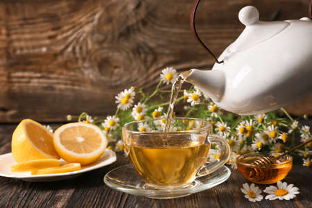 Pouring of chamomile tea from teapot into cup on tableの写真素材