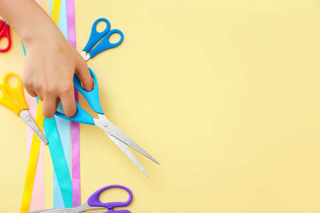 Female hand, scissors and ribbons on color background