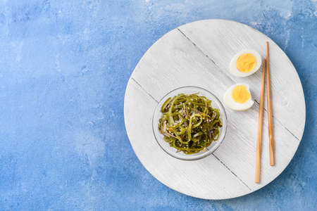 Bowl with tasty seaweed and boiled egg on color background
