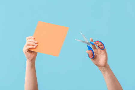 Female hands with scissors and paper sheet on color background