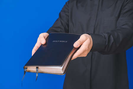 Young priest with Bible on color background, closeupの写真素材
