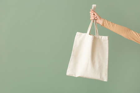 Female hand with eco bag on color background