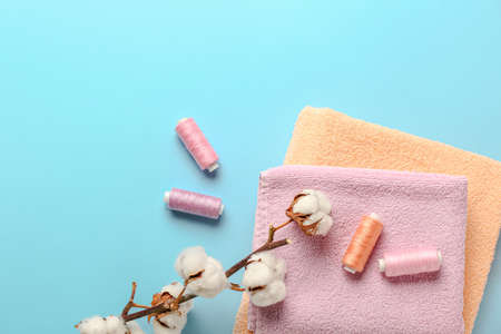 Cotton flowers, threads and soft towels on color background
