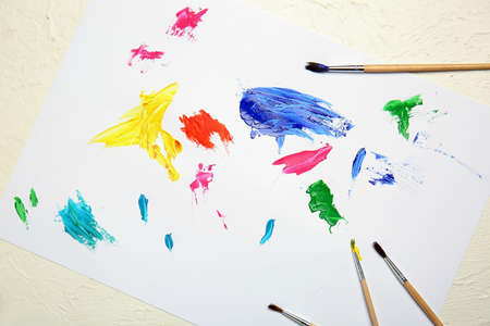 Paper sheet with paint strokes and brushes on tableの写真素材