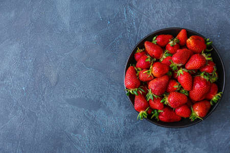 Bowl with fresh ripe strawberry on dark background