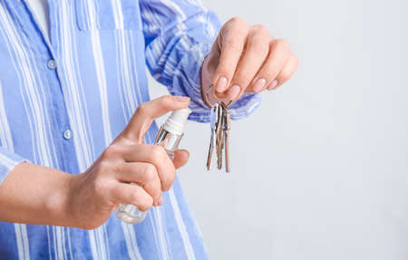 Woman disinfecting keys from house on gray backgroundの写真素材