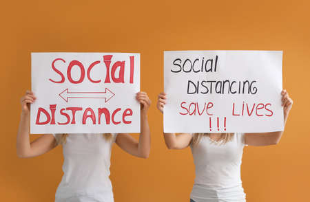Young women holding paper sheets on color background. Concept of social distance during coronavirus epidemicの写真素材